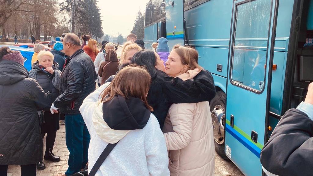 Menschen umarmen sich vor einem Reisebuss. 